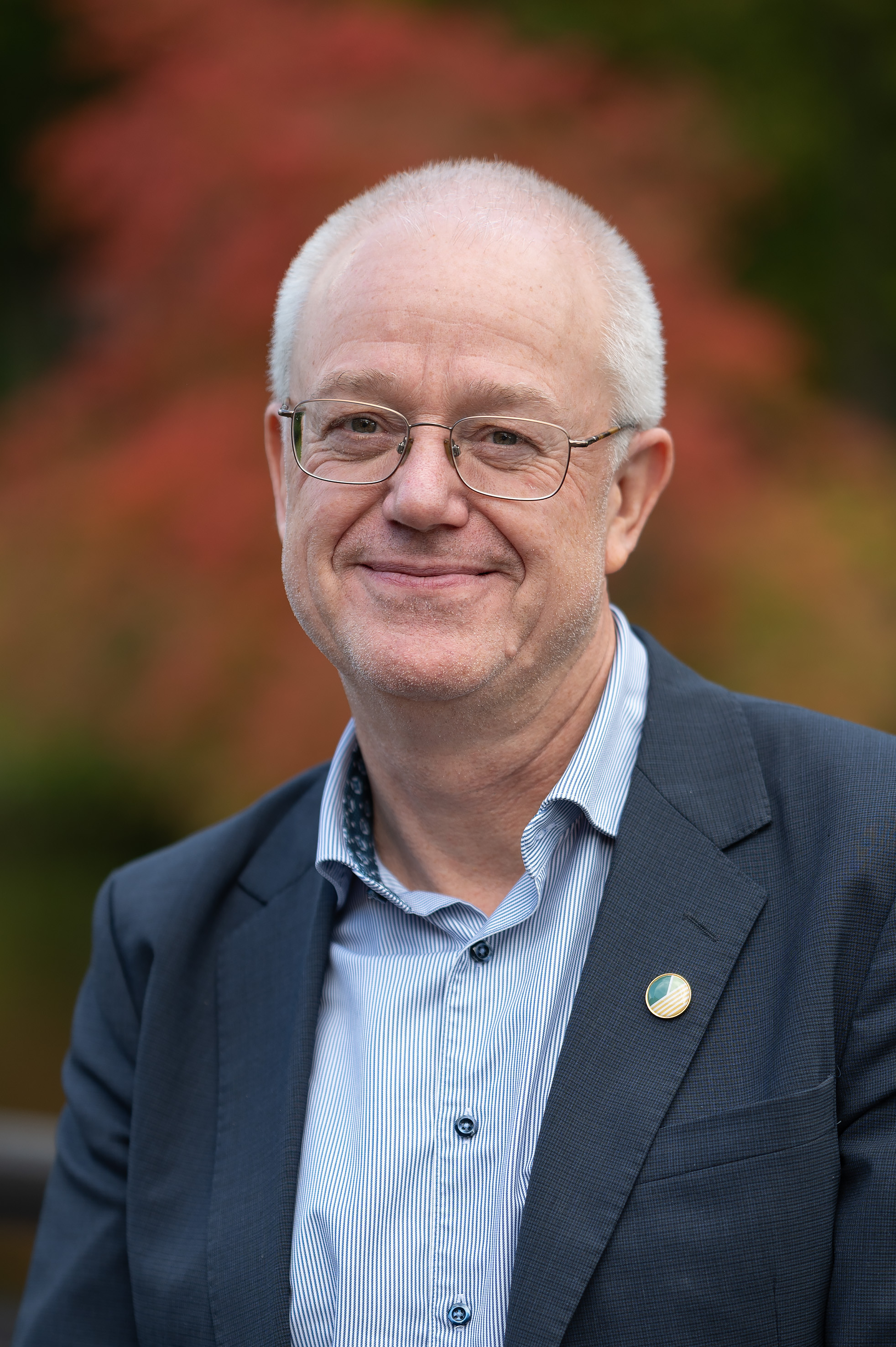 En man i kostym och glasögon ler mot kameran.